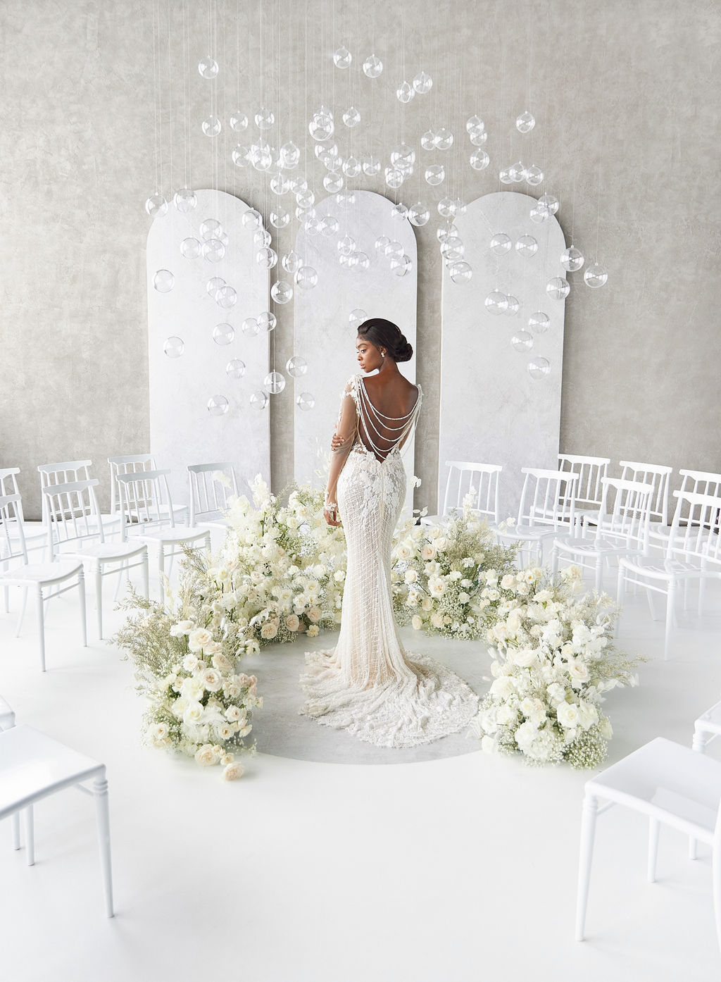 Bride posing in a wedding gown in the centre of the wedding ceremony setup surrounded by white flowers and chairs in a loft space